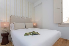 A neatly made bed with a book on it, a bedside lamp, and a striped wall. - Genteel Home Padre Marchena 13 202 (Seville)