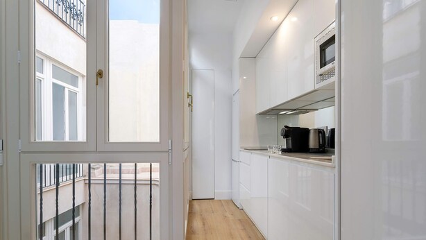 A narrow kitchen with white cabinets, a wooden floor, and a view of the outside through a glass door.