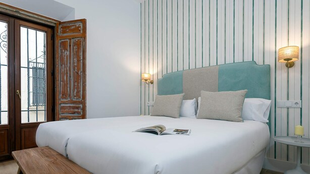 A neatly made bed with a magazine, a wooden bench, and a wall with vertical stripes. - Genteel Home Padre Marchena 13 101 (Seville)