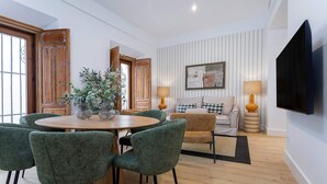 A modern living room with a round wooden dining table surrounded by green chairs, a sofa with checkered cushions, and a flat-screen TV mounted on the wall. - Genteel Home Padre Marchena 13 101 (Seville)