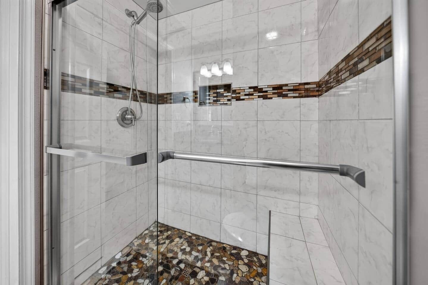 Une douche fermée par des parois en verre, dotée d’une barre d’appui, de murs carrelés et d’un sol recouvert de mosaïques.