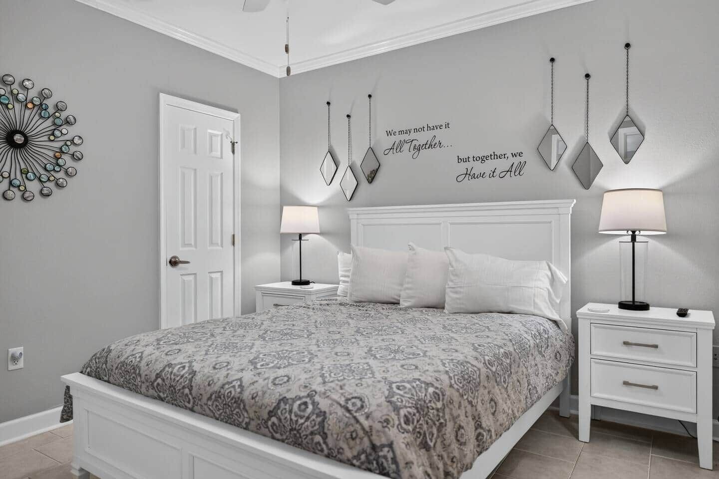 A bedroom with a bed, two bedside tables, a wall clock, and a decorative wall piece.