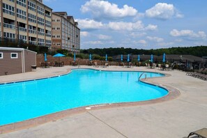 A swimming pool with lounge chairs and umbrellas, surrounded by a building with multiple floors and windows. - #217 Pointe - 2 Bedroom Lakefront Condo at Mariners SML (Bedford County)