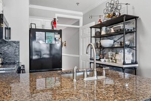 A kitchen with granite countertops, a stainless steel sink, a black refrigerator, and a black shelving unit with dishes. - #217 Pointe - 2 Bedroom Lakefront Condo at Mariners SML (Bedford County)