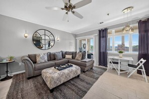 A modern living room with a sectional sofa, a patterned ottoman, a dining table with chairs, and a ceiling fan. - #217 Pointe - 2 Bedroom Lakefront Condo at Mariners SML (Bedford County)