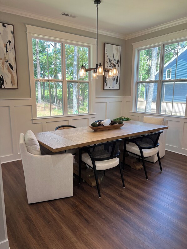 A dining area with a wooden table, white cushioned chairs, and a hanging light fixture.