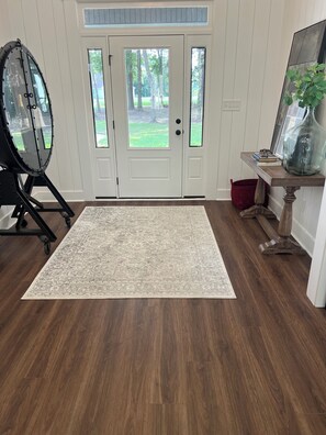 Una habitación con piso de madera, un tapete estampado, una puerta con paneles de vidrio y una mesa con un florero.