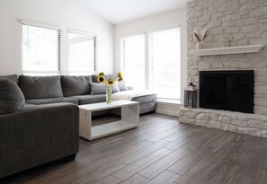 Un salon moderne avec un canapé gris, une table basse blanche et une cheminée en pierre.