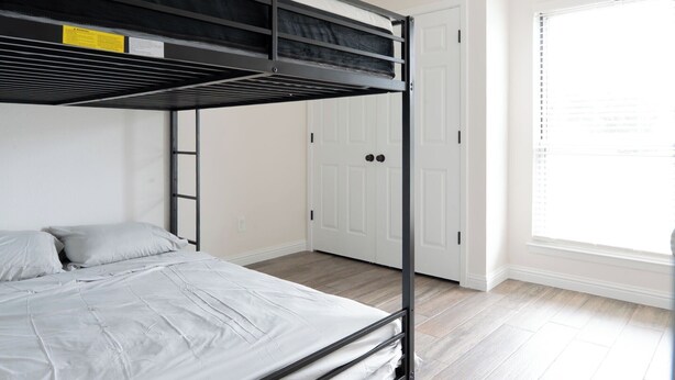 Una cama litera con escalera, una puerta blanca y una ventana con persianas.