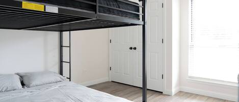 A bunk bed with a ladder, a white door, and a window with blinds.