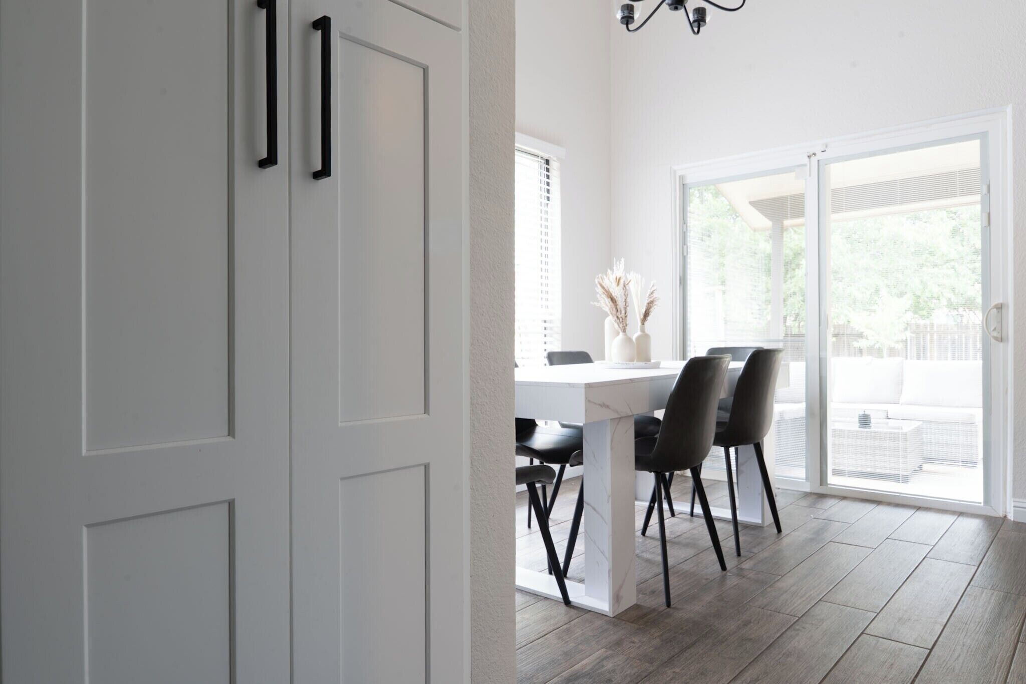 Un intérieur moderne avec un coin repas, des murs blancs et une vue à travers une porte vitrée.