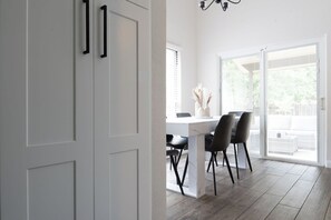 A modern interior with a dining area, white walls, and a view through a glass door.
