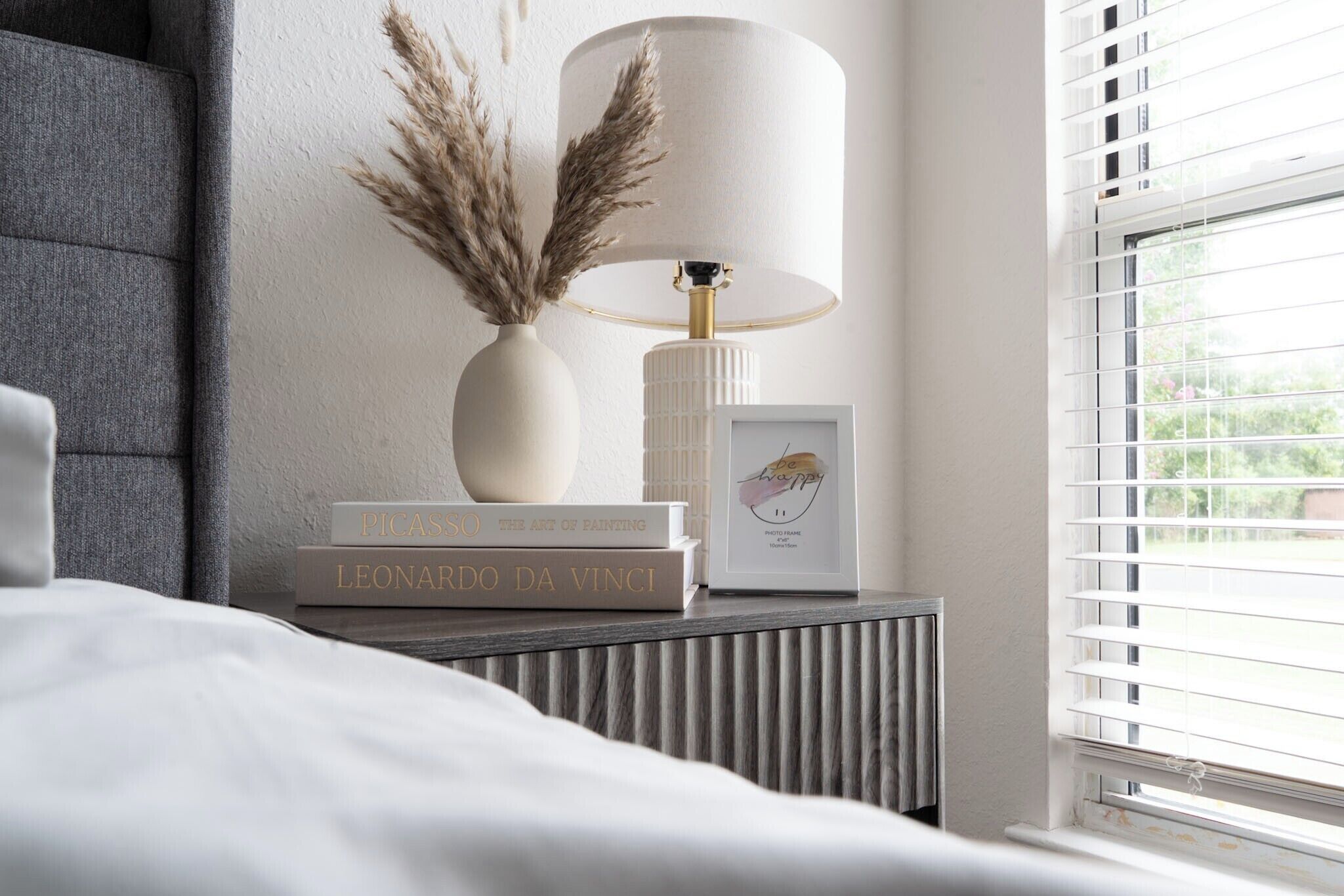 A neatly arranged bedside table with a lamp, a framed photo, and books.