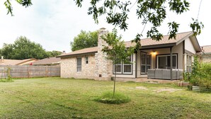 Propiedad residencial con fachada de piedra, un patio cubierto y patio trasero cercado.