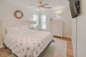 Ein Schlafzimmer mit einem Bett, einem Schminktisch, einem Nachttisch, einem Deckenventilator und einem an der Wand montierten Fernseher.