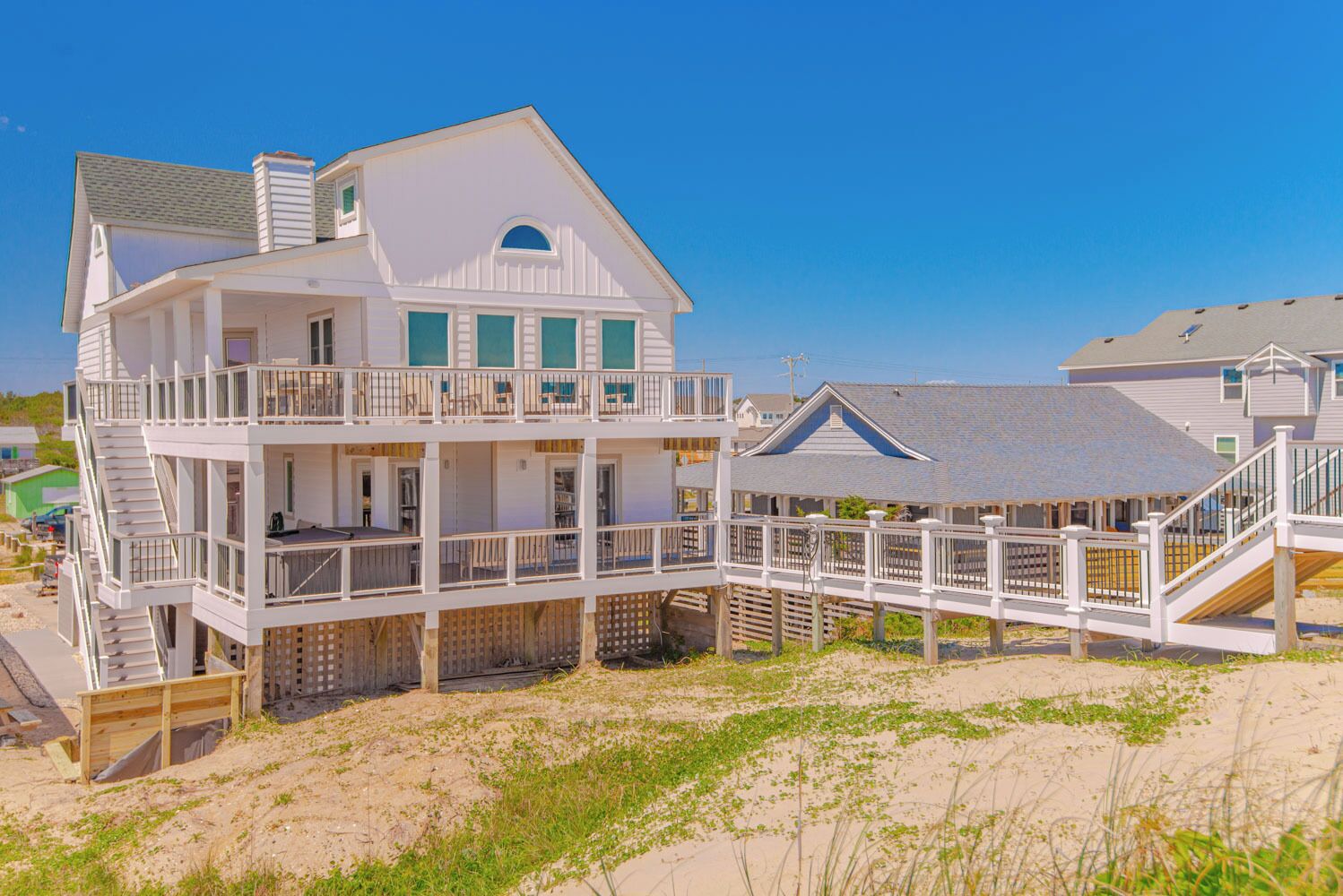 Une maison à plusieurs étages située en bord de mer, dotée d’un balcon, d’un escalier et d’une terrasse en bois.