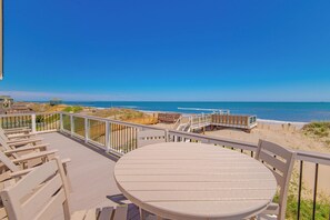 Une terrasse au bord de la plage, avec une table ronde et des chaises, des rampes en bois et une vue sur l’océan.