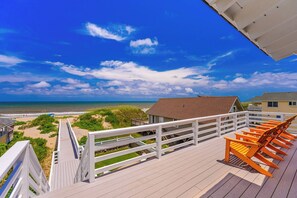 A wooden deck with a view of the beach and ocean, a building with a sloped roof, and a white railing. - JL #472 On the Rocks - Oceanfront - Pool - Hot tub (Nags Head)