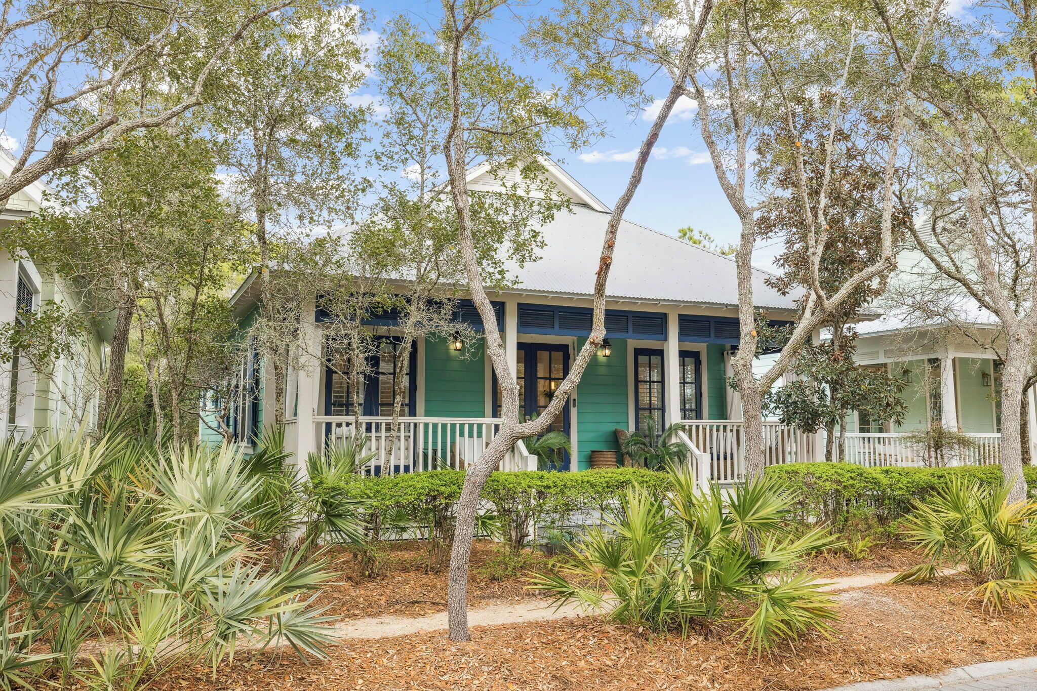 A two-story house with a porch, surrounded by trees and plants.