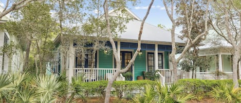 A two-story house with a porch, surrounded by trees and plants.