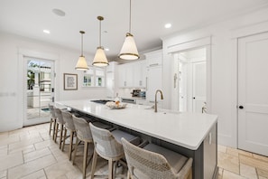 A modern kitchen with a large island, bar stools, pendant lighting, and a view of the outdoors. - Walk to Beach and Square | Private Pool (Inlet Beach)