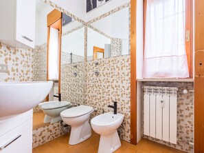 A bathroom with two toilets, a bidet, a sink, a mirror, and a radiator.