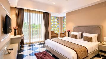 Habitación de hotel con una cama grande, televisión, escritorio con un florero y vista a zonas verdes por la ventana.
