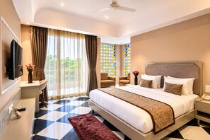 A hotel room with a large bed, a television, a desk with a vase of flowers, and a view of greenery through the window. - The HariMahal -A Luxury Hotel in Udaipur (Udaipur)