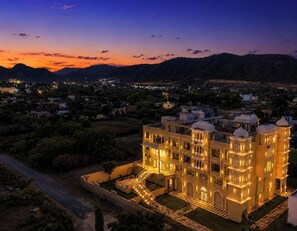 A large, illuminated building with multiple domes and arched windows, surrounded by a well-maintained garden and a view of distant hills. - The HariMahal -A Luxury Hotel in Udaipur (Udaipur)