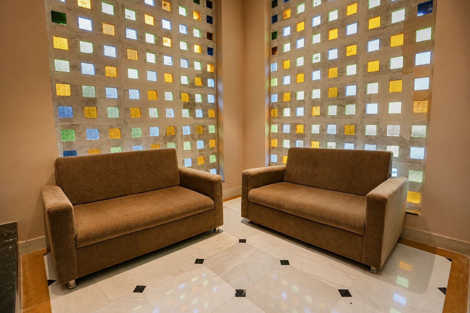 Dos sofás marrones en una habitación con suelo de baldosas y una pared con motivos cuadrados de colores.