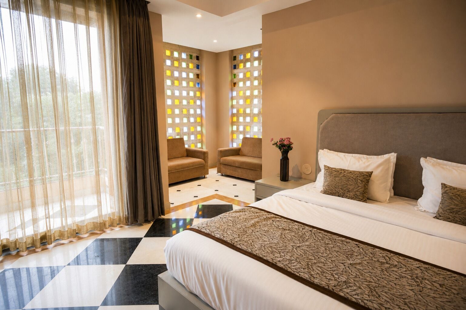 Une chambre d’hôtel comprenant un lit, deux fauteuils, une table de chevet et un mur décoratif agrémenté de jeux de lumière colorés.