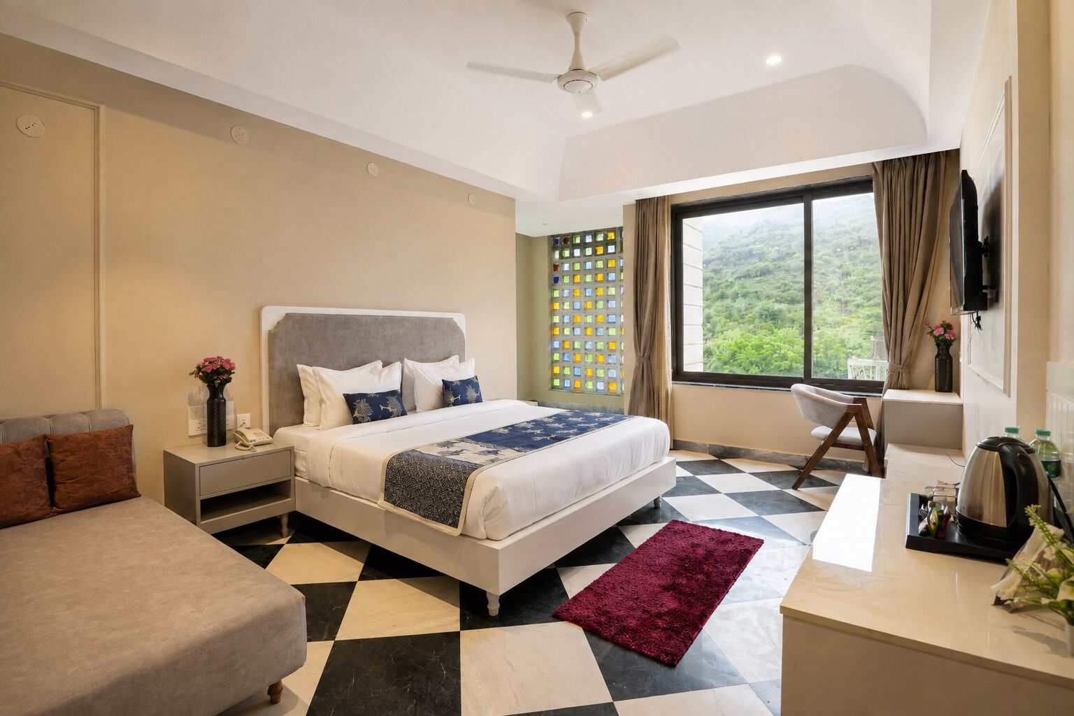 Habitación de hotel con cama, escritorio, silla, televisor y ventana con vista a vegetación.