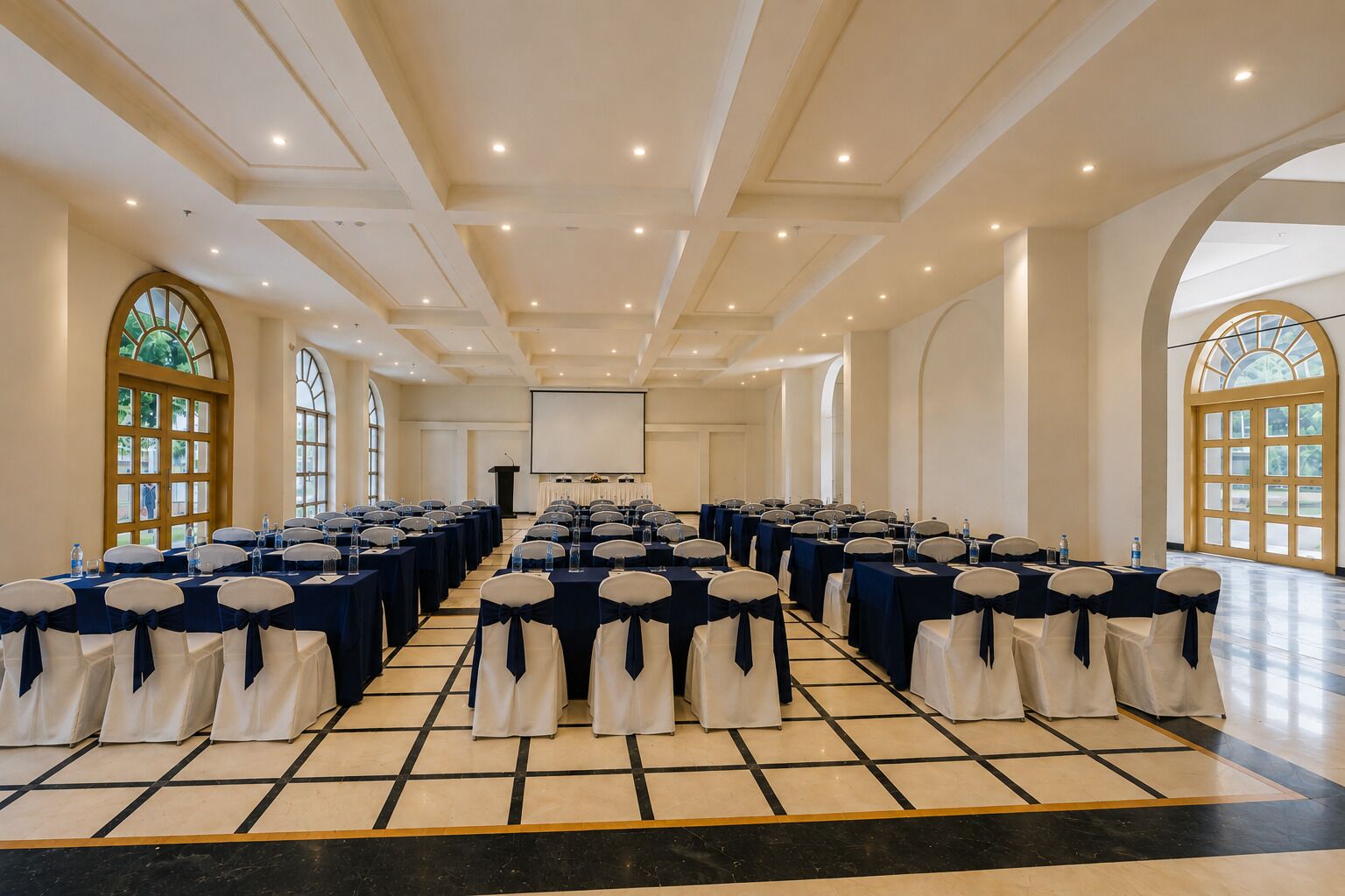 Une salle de conférence avec des rangées de tables et de chaises, un pupitre et de grandes fenêtres.