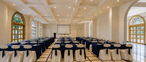 A conference room with rows of tables and chairs, a podium, and large windows.