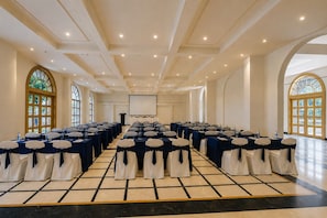 A conference room with rows of tables and chairs, a podium, and large windows.