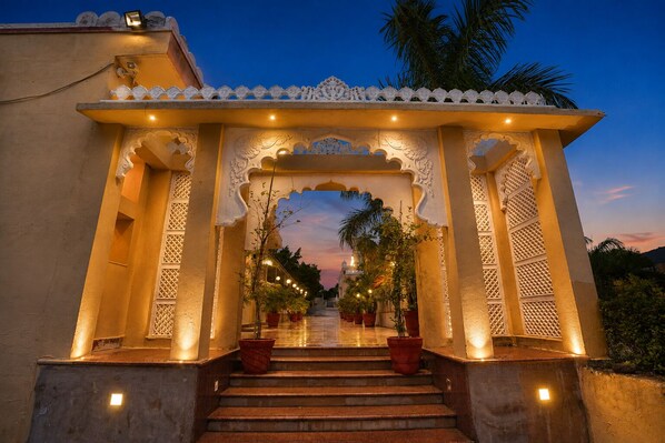 An ornate entrance with a staircase leading to a covered area, surrounded by potted plants and architectural details.