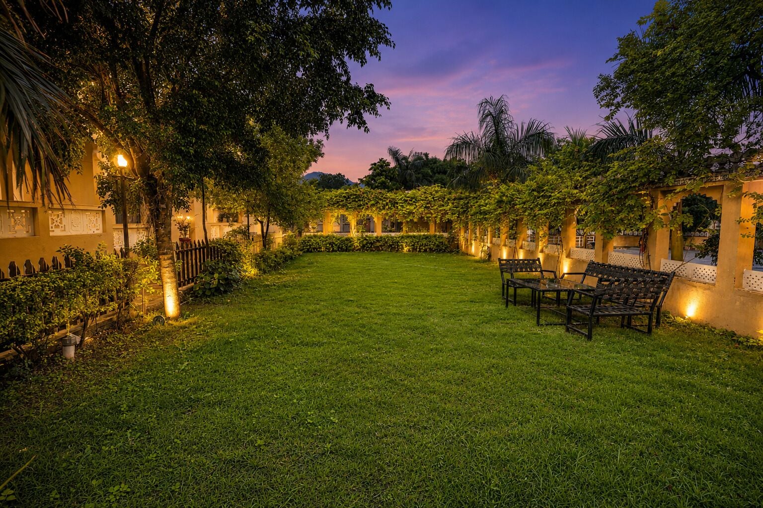 Un jardín bien cuidado con césped, zona de estar y un edificio con arcos e iluminación.