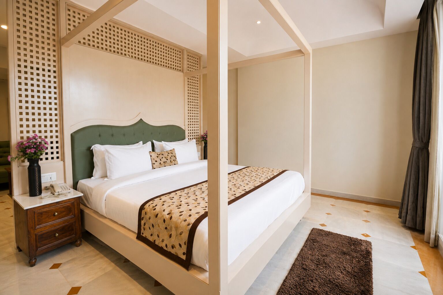 Habitación de hotel con cama con dosel, mesita de noche con un jarrón de flores y un amplio ventanal con cortinas.
