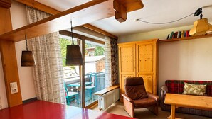 Eine Küche mit roter Arbeitsplatte, Holzbalkendecke, einem braunen Ledersessel, einem Holztisch und einem Fenster mit Vorhängen.
