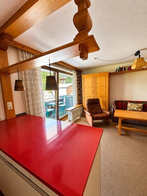 A kitchen with a red countertop, wooden ceiling beams, a brown leather chair, a wooden table, and a window with curtains. - Haus Stöckl Top 14 (Königsleiten)