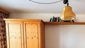 Una habitación con un armario de madera, un sillón de cuero, una mesa de madera y un sofá a cuadros con un cojín.