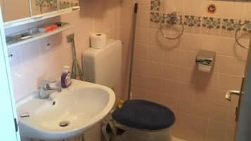 Baño con lavamanos blanco, inodoro, zona de ducha y espejo.