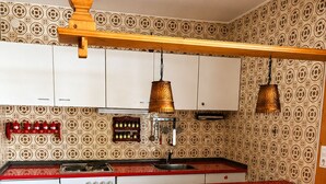Una cocina con encimera roja, dos taburetes de bar y papel tapiz estampado.