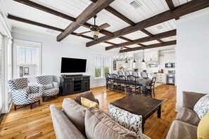 A spacious living room with a wooden floor, a dining area with a table and chairs, a kitchen with white cabinets, and a ceiling fan. - Marimac's Maison|Private Pool|Elevator|Golf Cart (Inlet Beach)