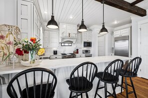 A modern kitchen with white cabinetry, a central island with bar stools, and pendant lighting. - Marimac's Maison|Private Pool|Elevator|Golf Cart (Inlet Beach)