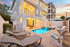 Ein zweistöckiges Haus mit Swimmingpool, Sitzgelegenheiten im Freien und einem gut beleuchteten Eingangsbereich.