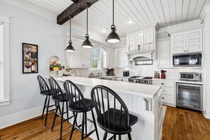 A kitchen with white cabinets, a central island with bar stools, a stove, and a microwave. - Marimac's Maison|Private Pool|Elevator|Golf Cart (Inlet Beach)