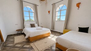 Un dormitorio con dos camas, suelo de madera y ventanas amplias.