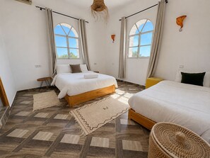 Ein Schlafzimmer mit zwei Betten, Holzboden und großen Fenstern.