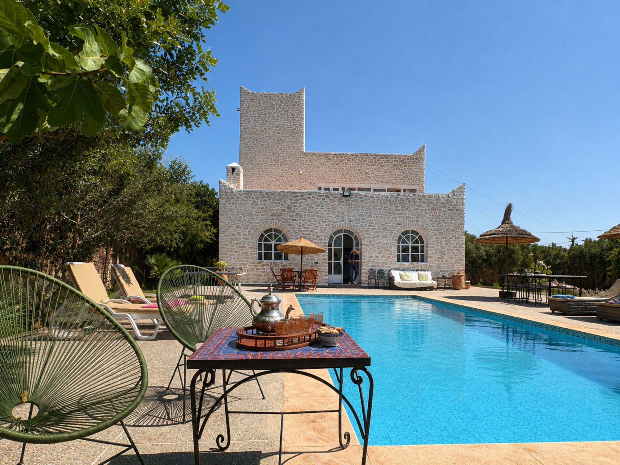 A stone building with a pool, outdoor furniture, and a clear sky.